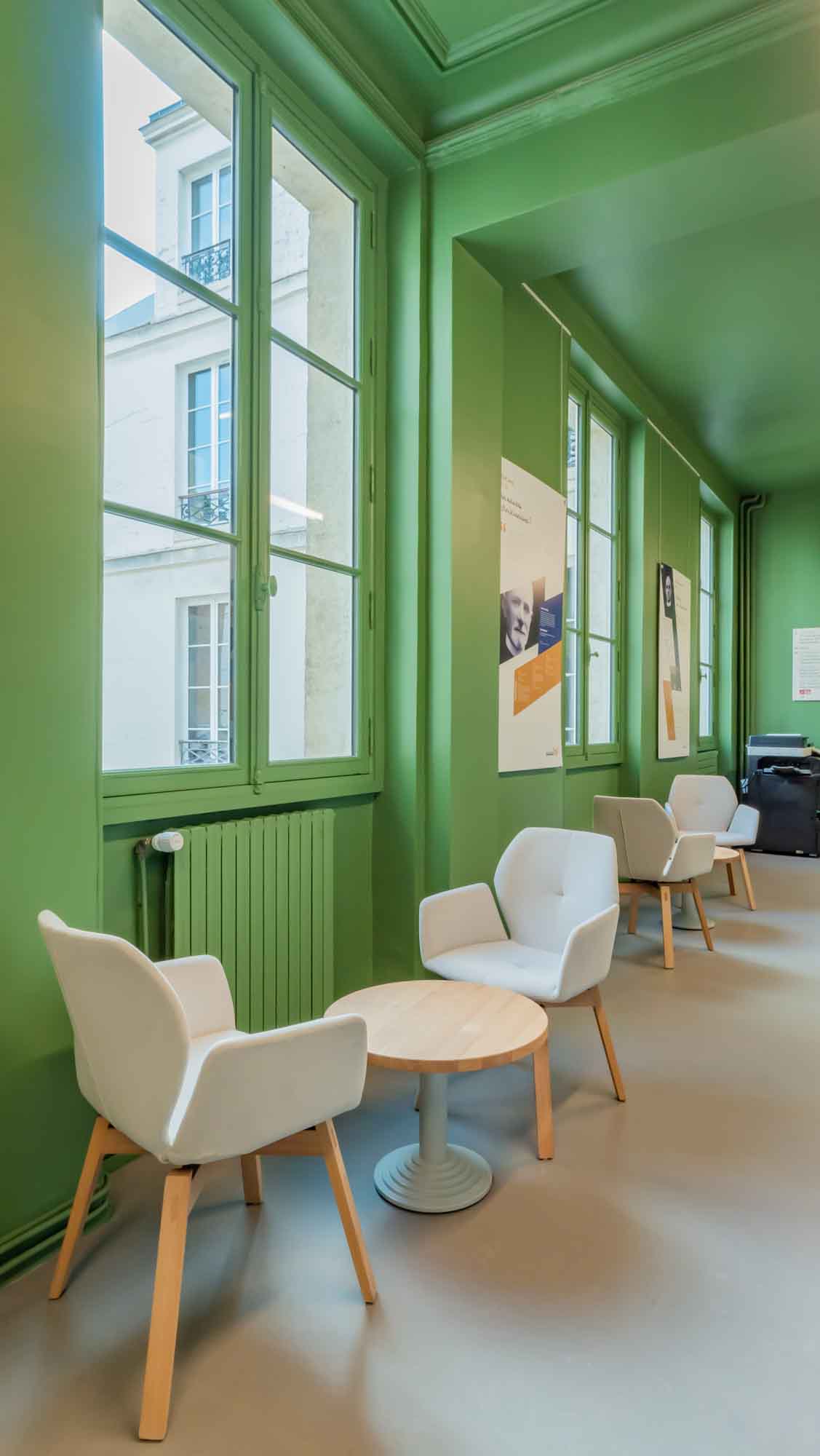 Salle d'attente de l'Institut Catholique de Paris, des petites tables et fauteuils dans une pièce verte et lumineuse.