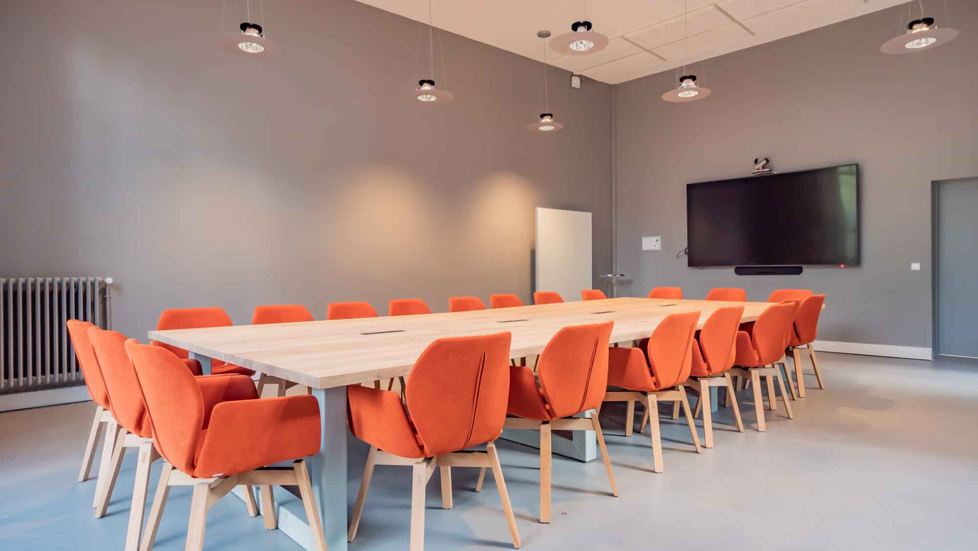 Grande salle de réunion, une table monumentale et ses fauteuils orange.