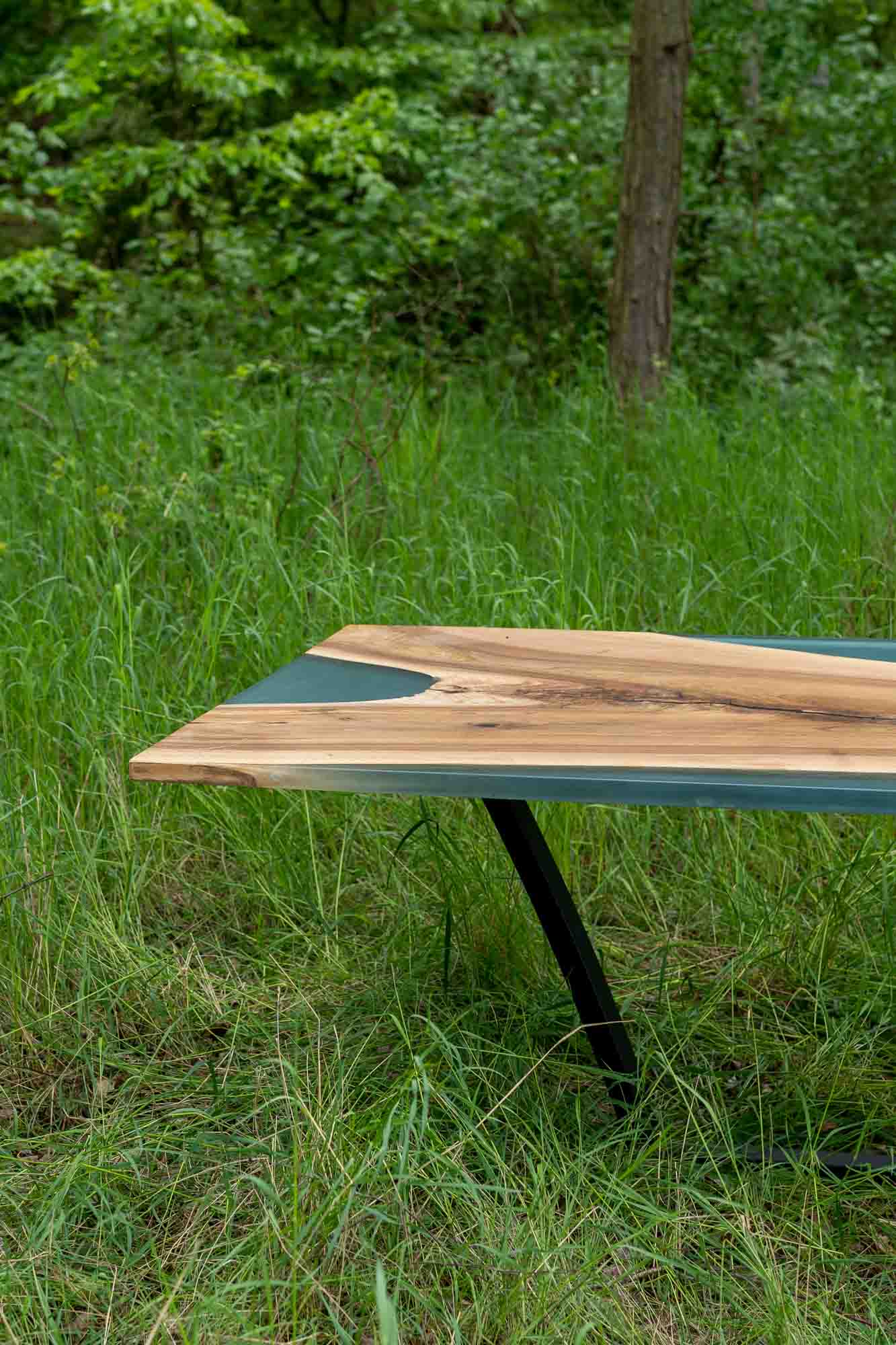 Table Indiana en orme et en résine époxy bleue dans son esprit sauvage entourée de verdure.